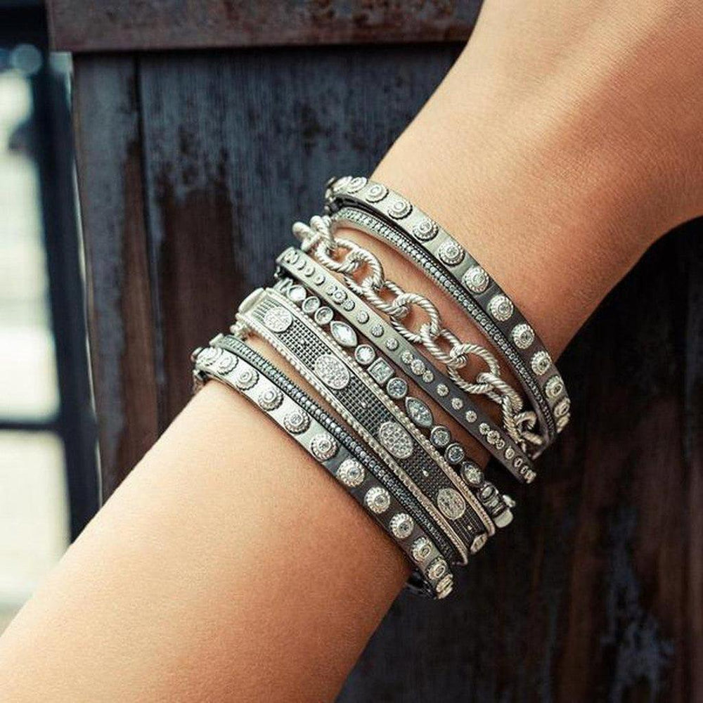 Stack of silver and dark gray bangles adorned with sparkling stones on a wrist.