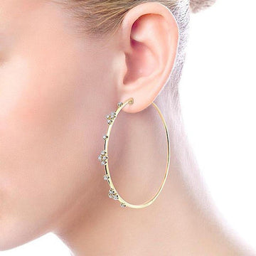 60mm gold hoop earrings adorned with tiny diamonds, shown on an ear.
