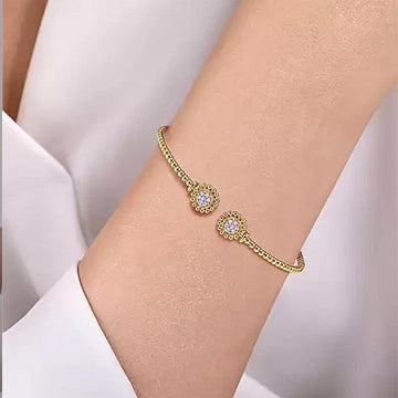 Gold open bangle bracelet adorned with pave diamond accents, shown on a wrist.
