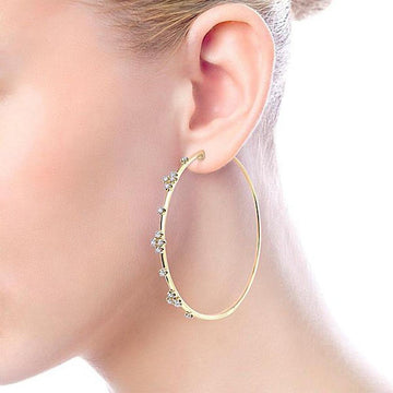 Large gold hoop earrings adorned with small diamonds, shown on an ear.
