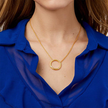 Gold circle pendant necklace with small diamonds, on a model wearing a blue shirt.
