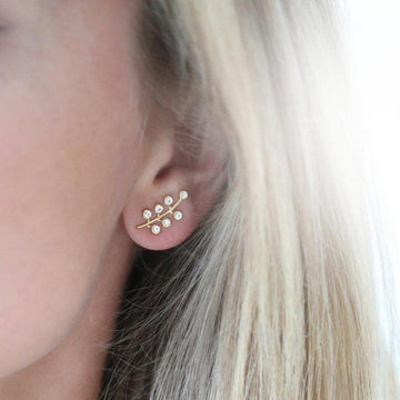 Gold leaf-design earrings with sparkling stones, worn on a model with blonde hair.
