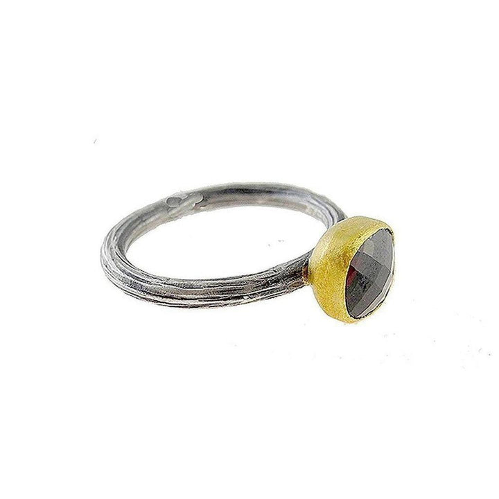 Dark garnet gemstone ring in gold setting, silver band with textured detail.
