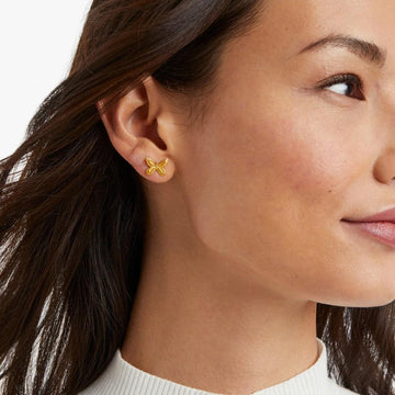 Gold butterfly stud earrings on a woman's ear.
