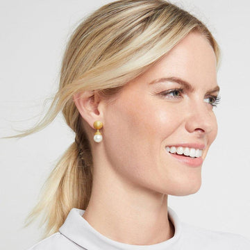 Gold and pearl drop earrings on a woman with blonde hair.
