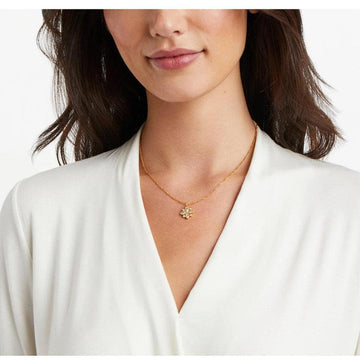 Gold chain necklace with delicate flower pendant; worn by model in off-white top.
