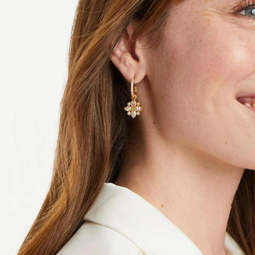 Gold hoop earrings with a sparkling floral charm, worn against a white background.
