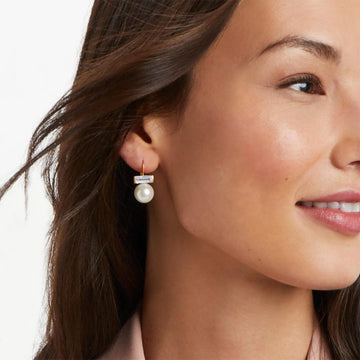 Gold-toned pearl and baguette-cut crystal drop earrings on a model.
