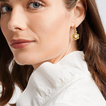 Gold flower earrings with a pearl center, worn by a woman in a white collared shirt.
