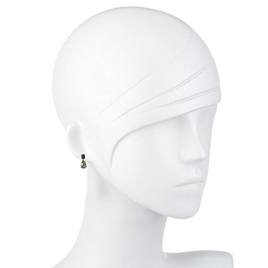 Elegant teardrop earrings displayed on a mannequin, featuring a dark stone and smaller accent.
