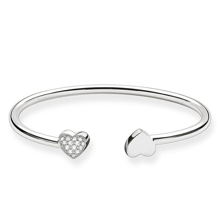 Silver cuff bracelet featuring two heart charms; one embellished with cubic zirconia.
