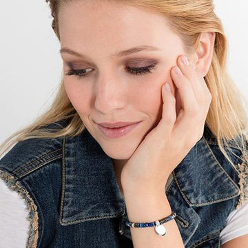 Woman's wrist wearing beaded bracelet with engravable charm; denim jacket backdrop
