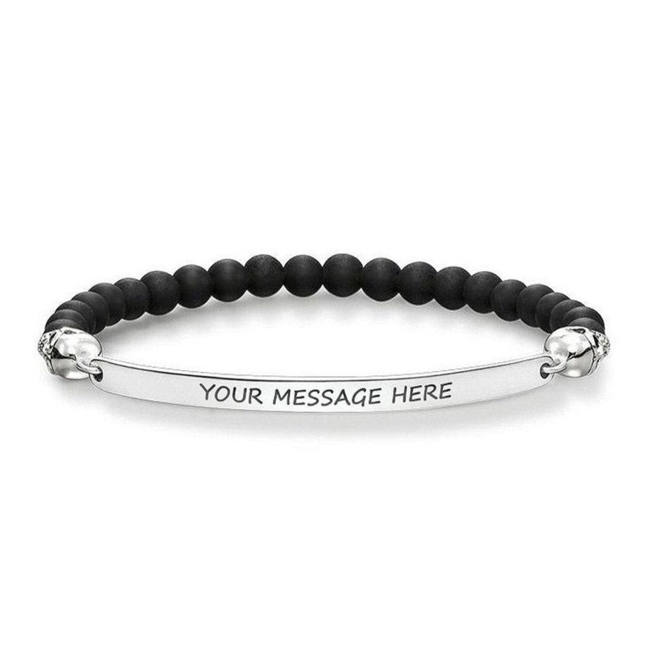 Black beaded bracelet with skull accents and engravable silver bar.
