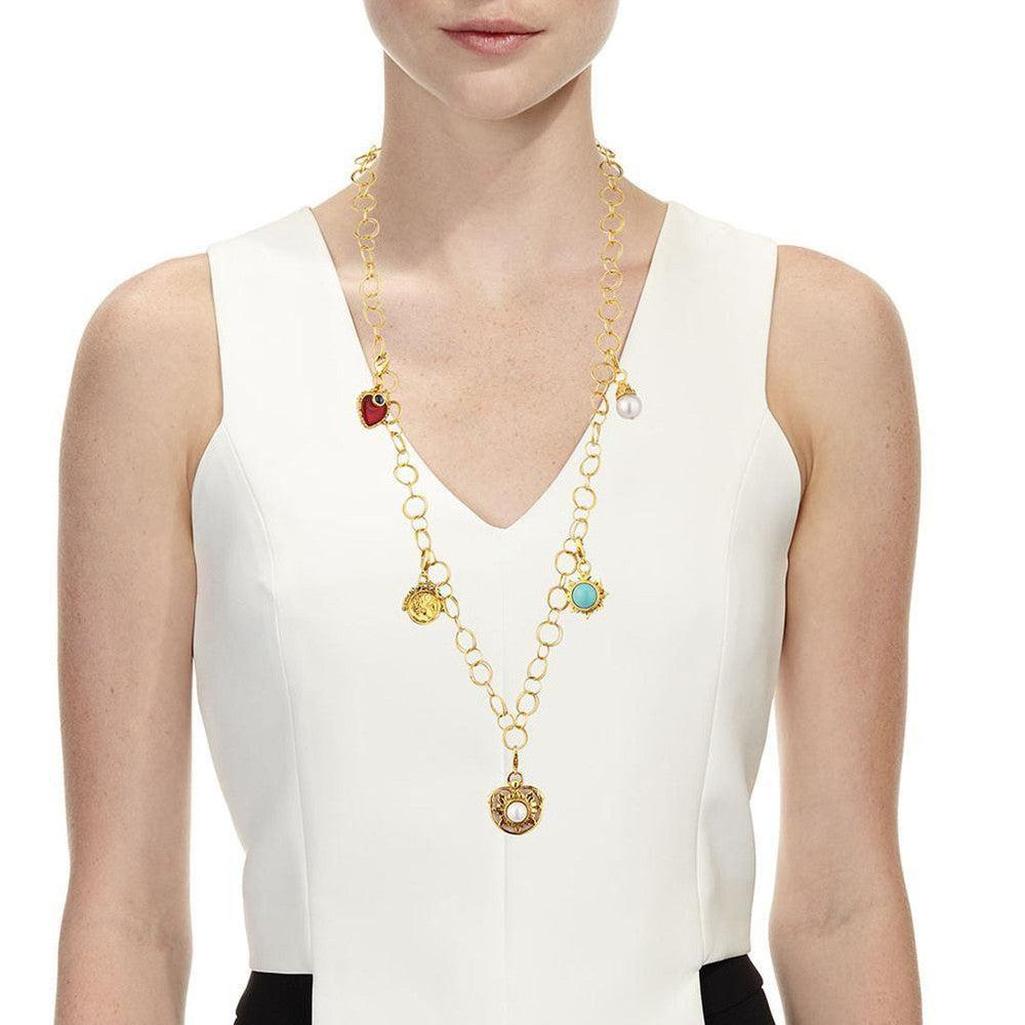 Gold multi-charm necklace featuring colored stones and a pearl, on a model.
