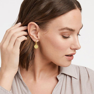 Gold fleur-de-lis charm earrings on model.
