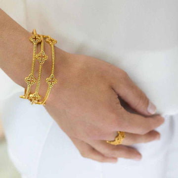 Gold bangle bracelet featuring clover accents, worn on a wrist.
