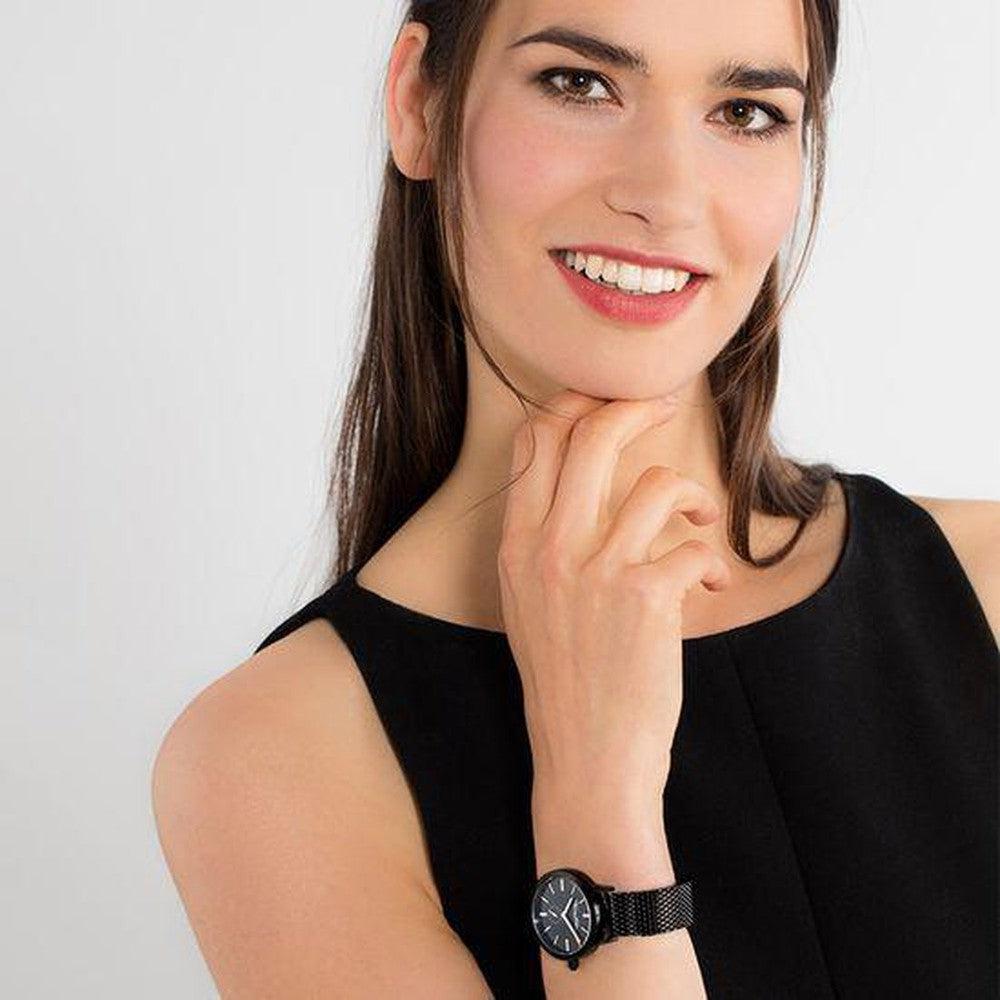 Woman's wrist showcasing a black mesh band watch with a simple, round face.

