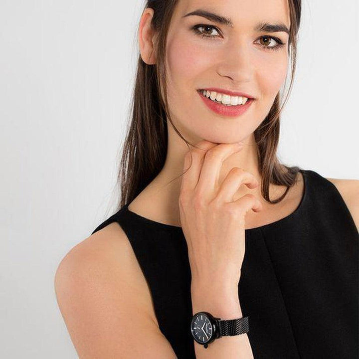 Woman's wrist showcasing a black mesh band watch with a simple, round face.
