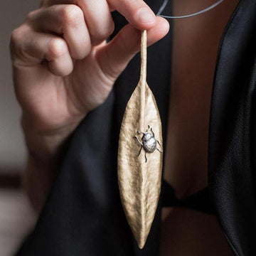Gold leaf pendant necklace featuring a silver insect detail.
