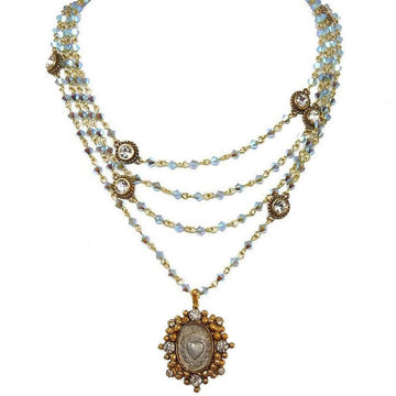 Layered iridescent blue crystal necklace with antique gold accents and a heart charm pendant.
