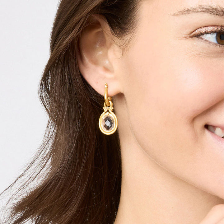 Saratoga huggie hoop earrings in 24K gold plate featuring a faceted crystal charm on a woman's ear.