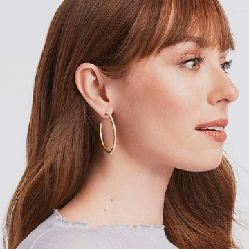Gold hoop earrings adorned with pearls, worn by a woman with long brown hair.

