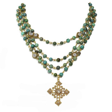 Layered turquoise bead necklace with ornate gold cross pendant.
