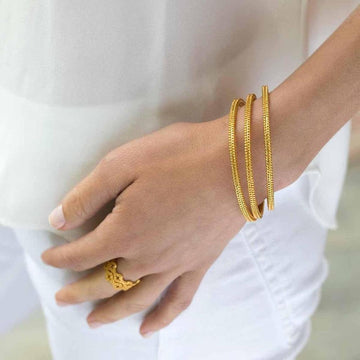 Gold bangles stacked on a wrist, detailed textured design.
