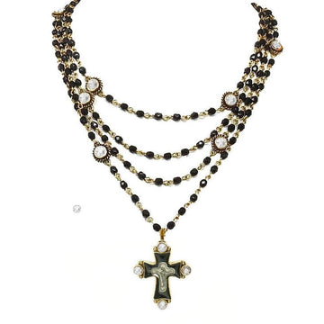 Multi-strand black bead necklace with gold accents and a cross pendant featuring clear stones.
