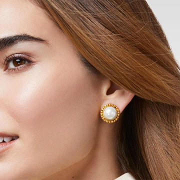 Close-up of gold pearl stud earrings on a woman's ear.
