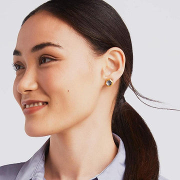 Woman wearing gold hexagonal stud earrings with gray stone accents.
