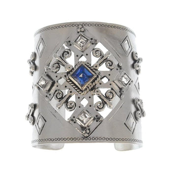 Silver cuff bracelet featuring an ornate design, blue sapphire, and clear stones.
