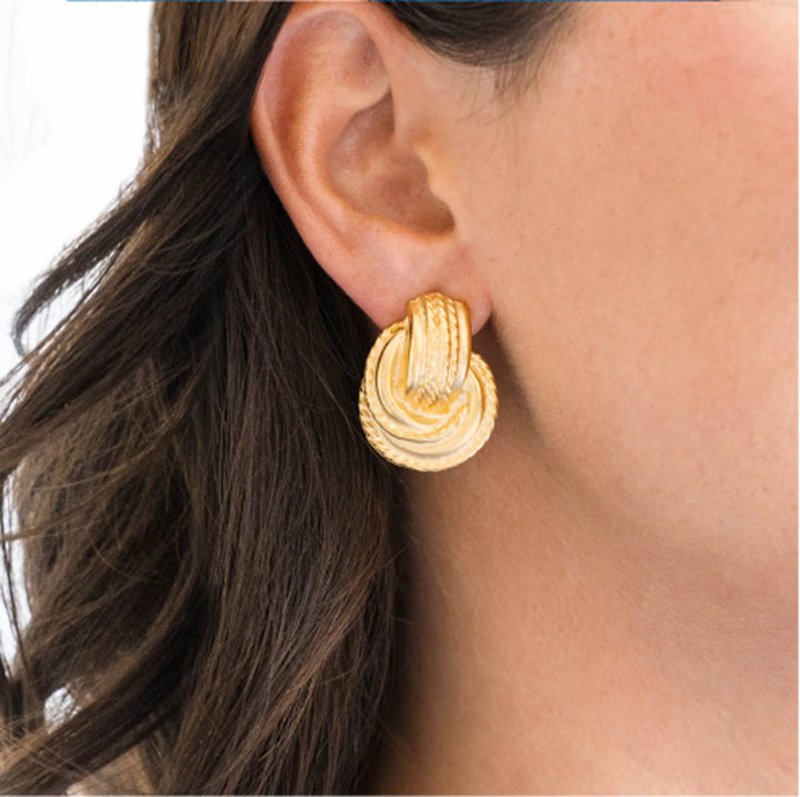 One-inch hand-cast gold-plated door knocker earrings with a textured circular design worn on an earlobe.