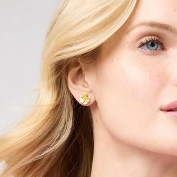 Gold flower stud earrings worn by a blonde woman.
