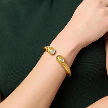Gold cuff bracelet featuring moonstone and quartz accents on a woman's wrist.
