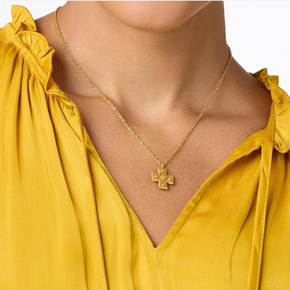 Gold cross necklace on a mustard yellow top.
