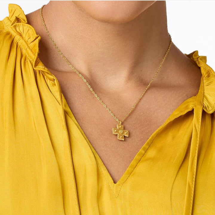 Gold cross necklace on a mustard yellow top.
