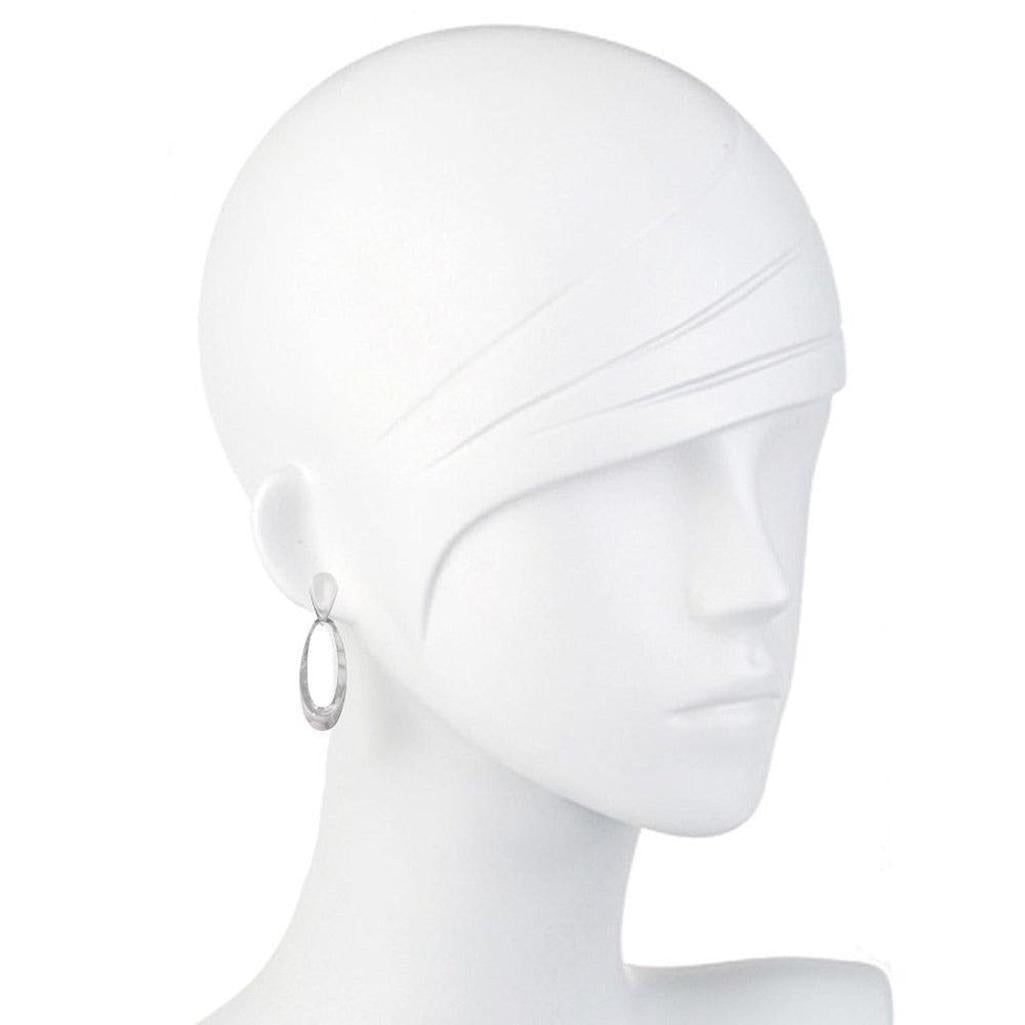 Silver elliptical earrings on a white mannequin.
