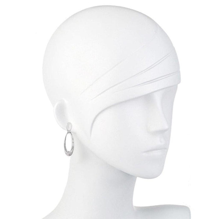 Silver elliptical earrings on a white mannequin.
