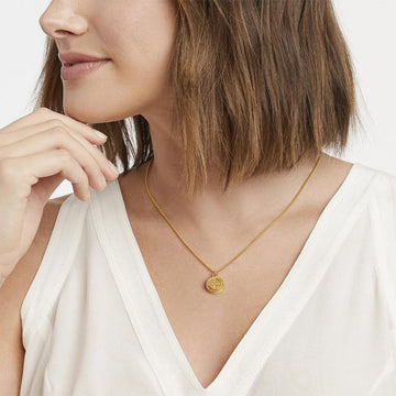 Gold fleur-de-lis pendant necklace on model wearing white top.
