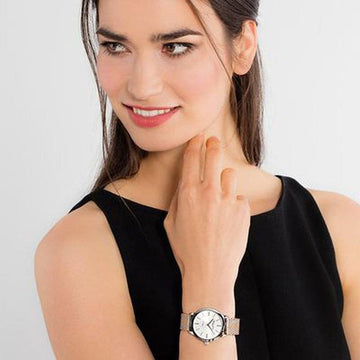 Woman's wrist showcasing a rose gold watch with a white face and mesh band.
