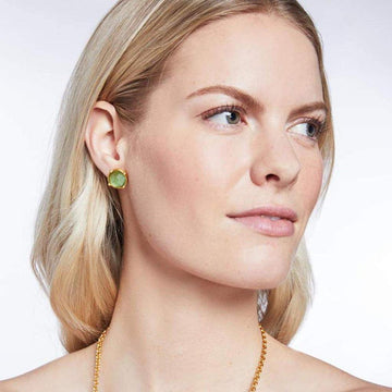 Green gemstone stud earrings in gold setting on model.
