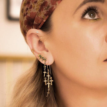 Gold cross earrings with dark green stones, dangling design.
