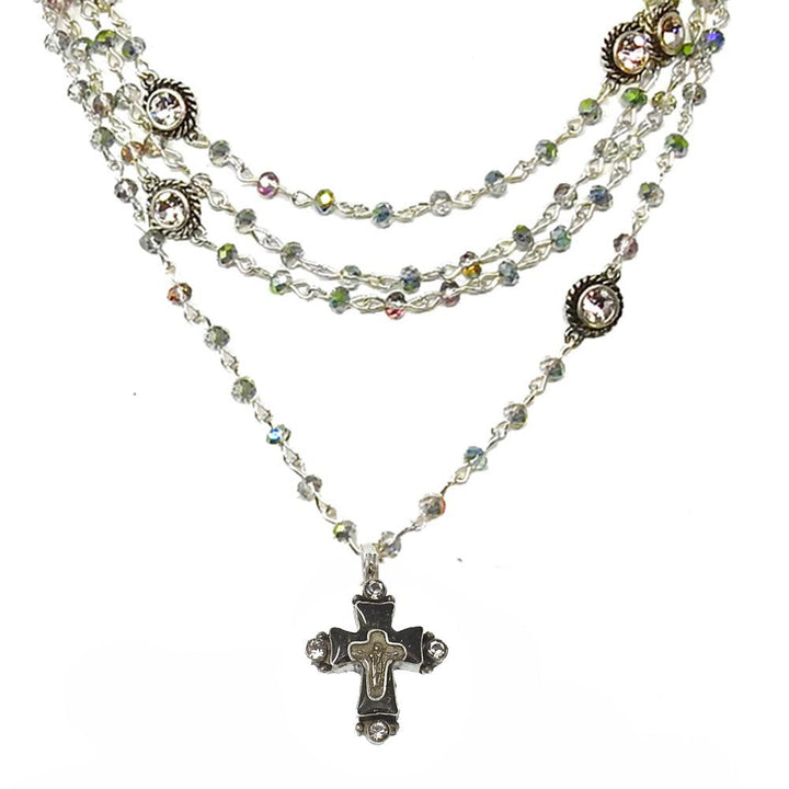 Layered silver necklace featuring a cross pendant and iridescent crystal accents.
