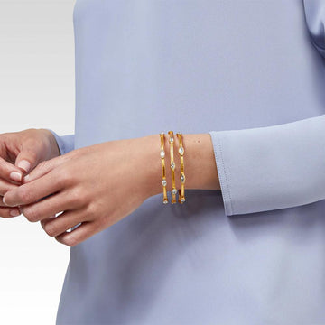 Gold bangles with clear stones, worn on a wrist.
